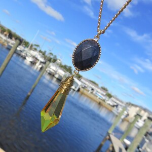 May include: A gold chain necklace with a black oval pendant and a yellow crystal teardrop pendant.