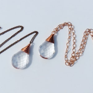 May include: Two crystal teardrop pendants on chains. The pendants are wrapped in copper wire and have a faceted design. The chain on the left is bronze and the chain on the right is gold.