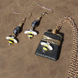 May include: A black lava rock pendant necklace with a gold chain and a small bee charm. Matching earrings with black beads and bee charms.