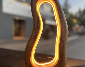 Könnte beinhalten: Eine Holzlampe mit einem warmen, orangefarbenen Schein, der aus der ausgehöhlten Form strahlt. Die Lampe ist aus Naturholz gefertigt und hat ein einzigartiges, organisches Design.