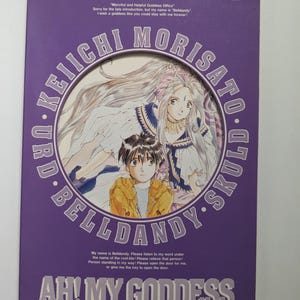 May include: A purple Ah! My Goddess postcard collection book featuring an illustration of Keiichi Morisato and Belldandy within a circular frame. The cover includes the text Post Card Collection, the names Keiichi Morisato, Urd, Belldandy, and Skuld.