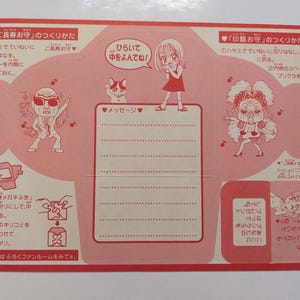 May include: A folded pink paper with Japanese text and illustrations. The paper features cartoon characters, instructions, and a space for a message. The design includes hearts, musical notes, and a cat.