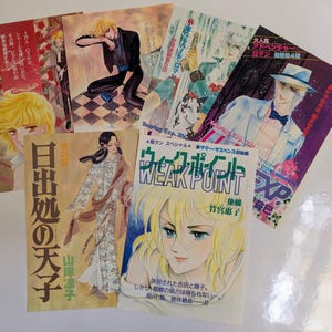 May include: A collection of Japanese manga comic books with colorful illustrations. The covers feature various characters, including a blonde woman and a man in a suit. Text in Japanese is visible on the covers.