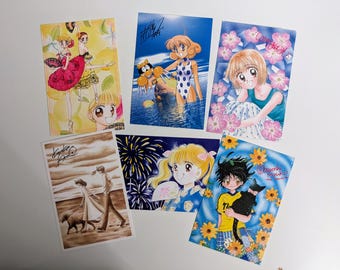 May include: A set of ten trading cards featuring anime characters. The cards are colorful and feature a variety of characters, including a girl with pink hair, a girl with blue hair, and a girl with blonde hair. The cards also feature a variety of backgrounds, including a beach, a forest, and a city.