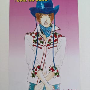 Pu&ograve; includere: Illustrazione di una persona con cappello da cowboy blu, camicia bianca con dettagli di fragole e bandana blu. Il testo "UME NO SONO" &egrave; in alto. L'immagine &egrave; firmata da Momota Nakahara, Kadokawa Shoten, ASUKA 1997.