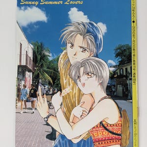 Könnte beinhalten: Ein Manga-Cover mit dem Titel "Sunny Summer Lovers". Das Bild zeigt zwei Charaktere im Anime-Stil vor einem blauen Himmel und einer Straßenszene. Japanischer Text ist ebenfalls vorhanden.