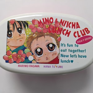 Könnte beinhalten: Weiße, ovale Lunchbox mit Anime-Illustrationen von zwei Kindern und floralen Akzenten. Der Text enthält "MINO & NIICHA LUNCH CLUB" und "It's fun to eat together! Now let's have lunch".