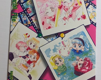 May include: A pink and green book with the title "Memorial File" on the cover. The cover features illustrations of anime characters from the Sailor Moon series.