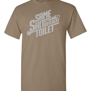 Puede incluir: Una camiseta de color marr&oacute;n claro con un gr&aacute;fico blanco que dice "Same Shit Different Toilet" con una llave inglesa y un gr&aacute;fico de inodoro.