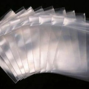 May include: A stack of clear, transparent plastic zip-top bags. The bags are rectangular with a zip closure at the top. The bags are arranged in a fan shape, with the top edges aligned.