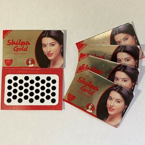 May include: A pack of black bindi stickers with a red and gold box featuring the text "Shilpa Gold" and a woman with a bindi on her forehead.