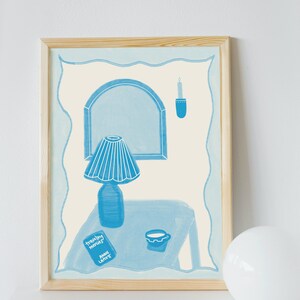 May include: A framed illustration of a blue lamp, a book titled "travelling notes" by Annie Laird, a cup, and a candle on a table. The illustration is set against a light blue background.