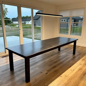 May include: A dark brown rectangular dining table with four sturdy legs. The table is made of wood and has a smooth, polished surface. The table is approximately 10 feet long.