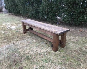 May include: A rustic wooden bench with a dark brown stain. The bench has a simple design with a single plank top and two sets of legs.