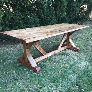 May include: A rustic wooden table with a natural wood finish and a trestle base. The table is made of reclaimed wood and has a distressed look. It is perfect for a farmhouse or industrial style home.