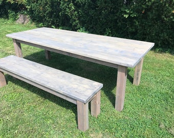 Könnte beinhalten: Ein rustikaler Holztisch und eine Holzbank in grau gewaschener Ausführung. Der Tisch ist lang und rechteckig mit einem einfachen Design. Die Bank ist kürzer und hat ein ähnliches Design. Beide Teile sind aus massivem Holz gefertigt und haben eine verwitterte Optik.
