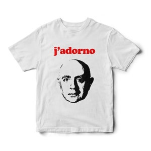 May include: White t-shirt with a black and white image of a man's face and the text "j'adorno" in red.