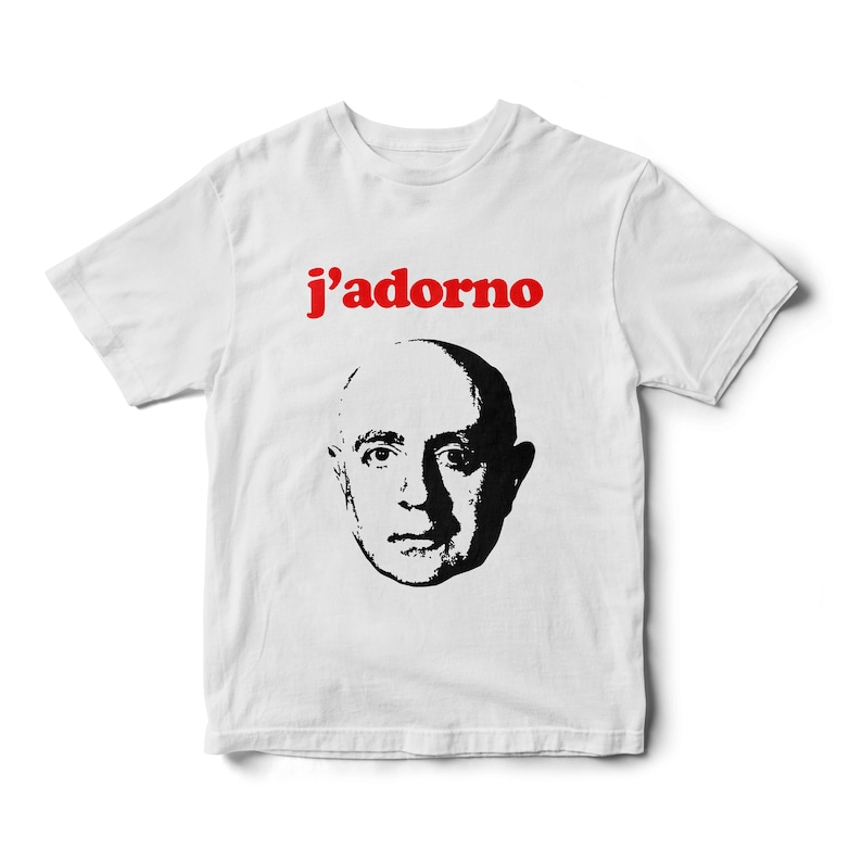 May include: White t-shirt with a black and white image of a man's face and the text "j'adorno" in red.
