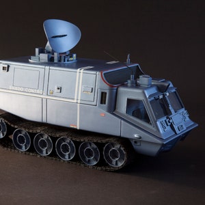 May include: A gray model of a tracked vehicle with a radar dish on top. The vehicle has a sign that reads "SHADO CONTROL".
