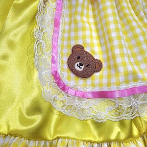 Yellow dress with pink trim, lace, and a teddy bear patch.