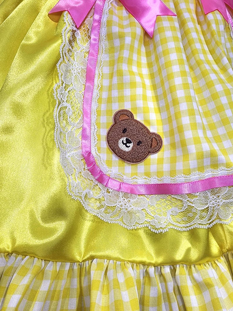 Yellow dress with pink trim, lace, and a teddy bear patch.