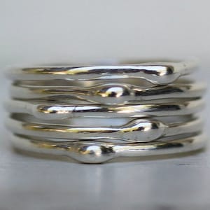 Peut inclure: Une bague en argent composée de plusieurs bandes fines aux bords arrondis. Chaque bande a une petite perle ronde au sommet.