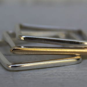 May include: Three square-shaped rings stacked on top of each other. The top two rings are silver and the bottom ring is gold.