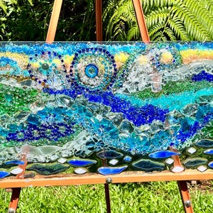 May include: A rectangular glass mosaic art piece featuring a vibrant landscape of blue, green, and yellow crushed glass fragments. The composition includes swirling circular patterns, textured layers of sea glass, and distinct blue and white glass shapes.