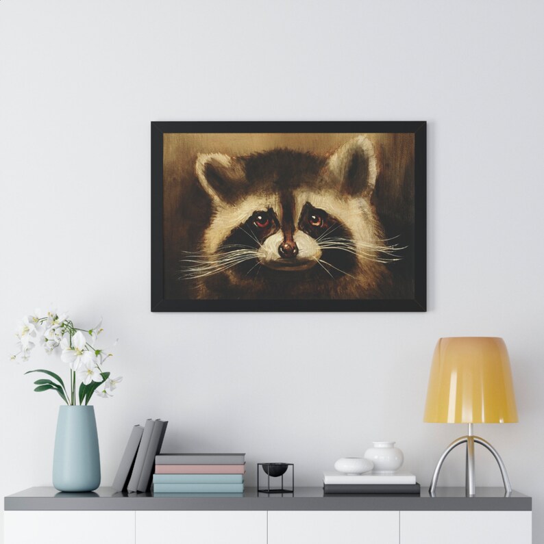 May include: A framed painting of a raccoon's face. The raccoon has brown fur, a black nose, and black eyes. The background is a dark brown color.