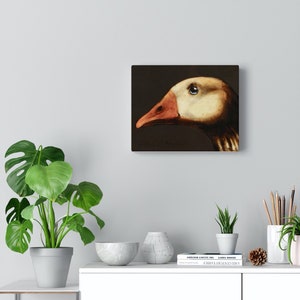 May include: Square canvas art featuring a detailed painting of a goose's head in profile. The goose has a cream-colored head, a reddish-orange beak, and a dark eye. The background is a deep, dark brown. The artist's signature is visible.