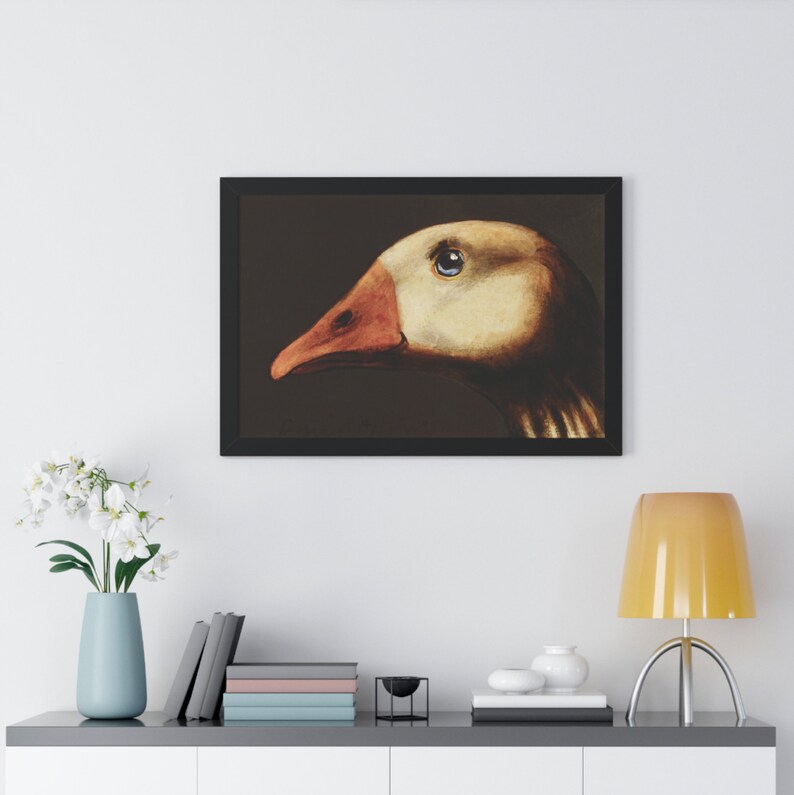 May include: Framed art print featuring a detailed illustration of a goose's head in profile. The artwork showcases the goose's eye, beak, and feathers with a focus on color and texture. The goose has a beige head and a reddish-orange beak. The artwork is framed in a black frame.