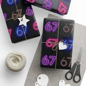Pode incluir: Papel de embrulho preto com um padrão de néon "67" em rosa e azul. Os presentes embrulhados são amarrados com barbante e adornados com etiquetas brancas em forma de estrela e coração. Uma bola de barbante, tesouras e etiquetas em branco também são visíveis.