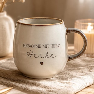 May include: A round, off-white ceramic mug with a speckled finish and a brown rim. The text HEBAMME MIT HERZ is printed in black, followed by the name Heike in a cursive script and a small black heart icon centered below the name.
