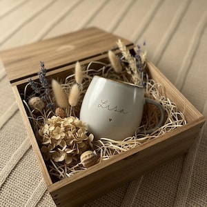 May include: A wooden gift box with a light gray mug that has the name "Lisa" written on it in cursive with a small heart. The mug has a gold rim and is surrounded by dried flowers and straw. The box is open.
