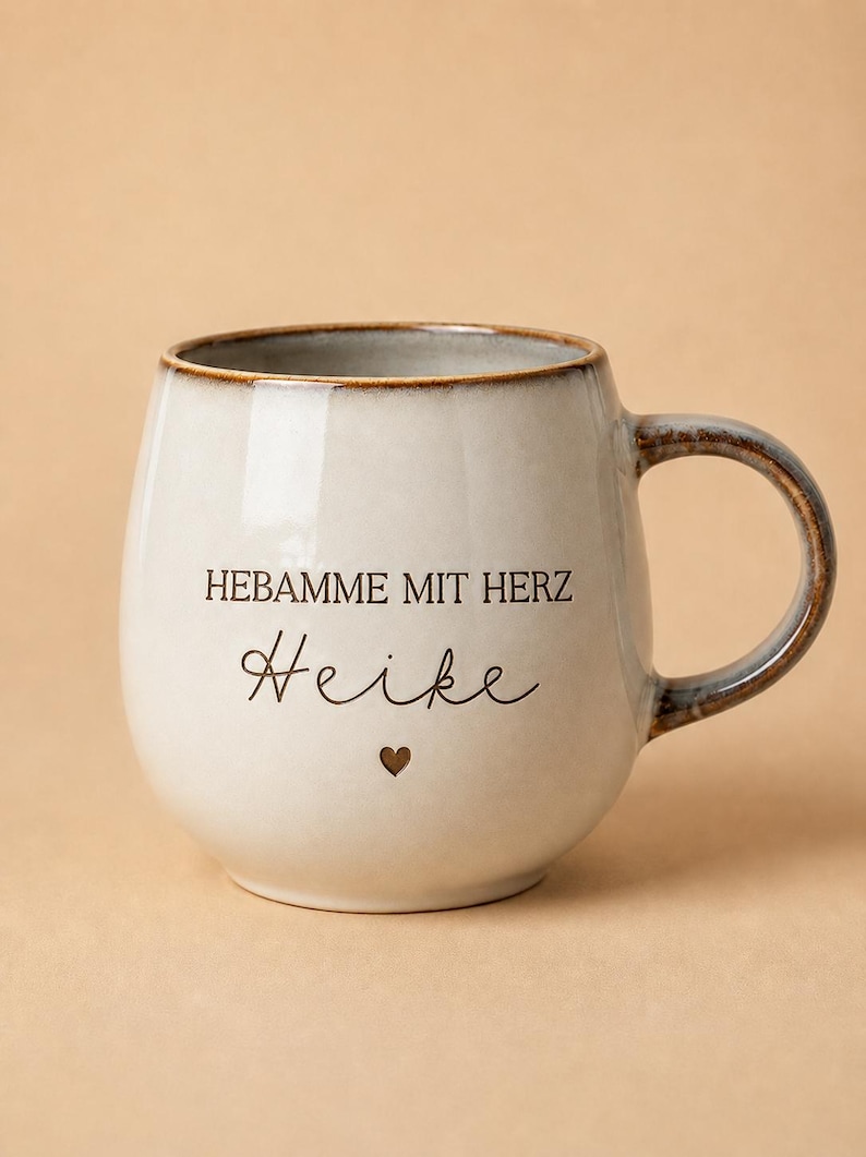 May include: A ceramic mug with a rounded shape, featuring a cream-colored glaze with a brown rim and handle. The text HEBAMME MIT HERZ and the name Heike are printed in black, accompanied by a small brown heart icon centered below the name.