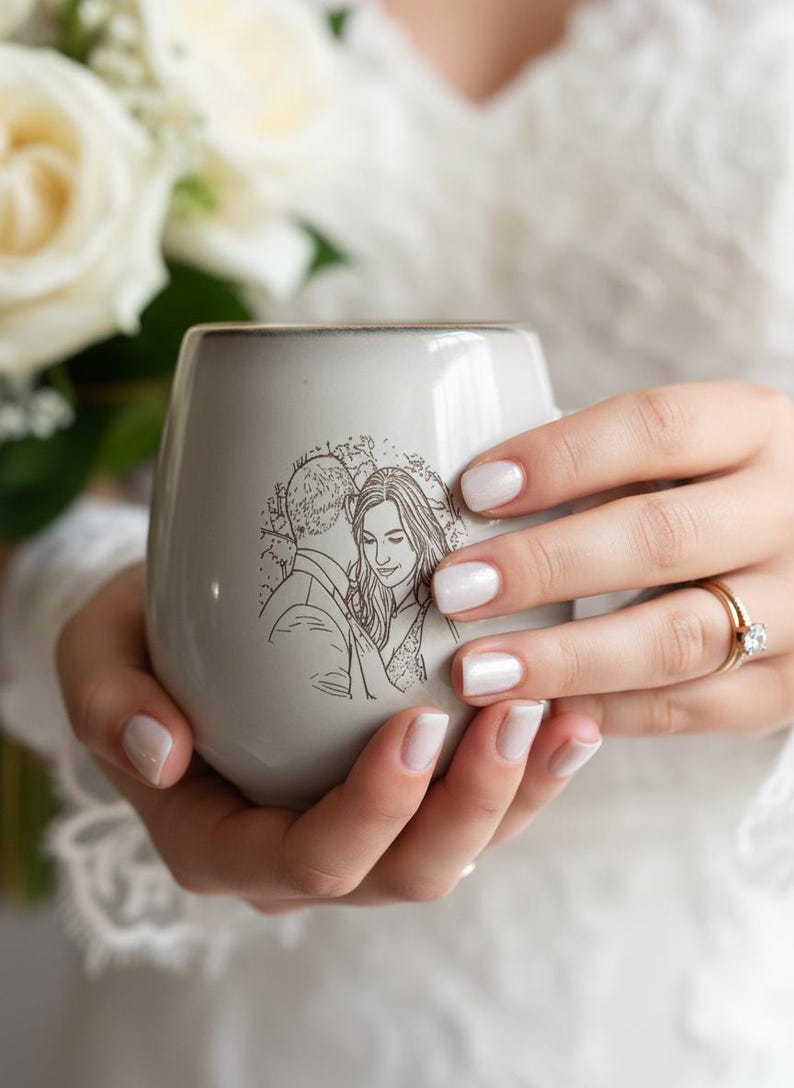 May include: A light gray ceramic mug featuring a dark brown line art illustration of a couple embracing. The mug has a smooth, rounded shape with a subtle gradient near the rim, showcasing a detailed sketch of two people in a close, intimate pose.