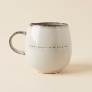 May include: A white ceramic mug with a rounded shape and a dark brown rim. The mug has a curved handle and features the handwritten text "Sch&ouml;n, dass es Dich gibt!" in black. A simple and elegant design.
