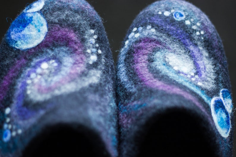 May include: A pair of dark blue wool slippers with a galaxy-themed design. The slippers feature white, blue, and purple swirls and dots, resembling a nebula.