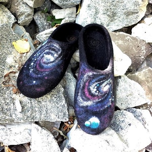 May include: A pair of black wool slippers featuring a galaxy design. The slippers have a swirling pattern of blue, pink, and white, with white dots representing stars.