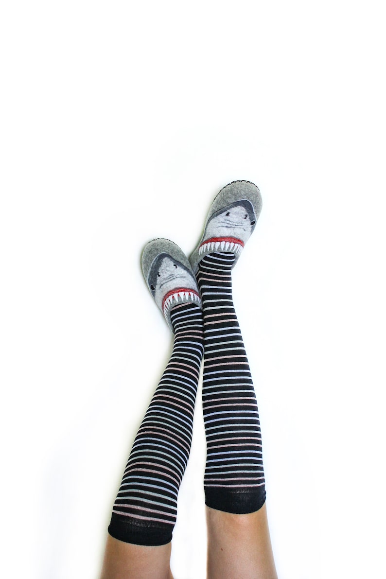 Pu&ograve; includere: Un paio di calze a righe bianche e nere fino al ginocchio con un design a forma di squalo sulle dita. Le calze sono indossate sulle gambe di una persona.