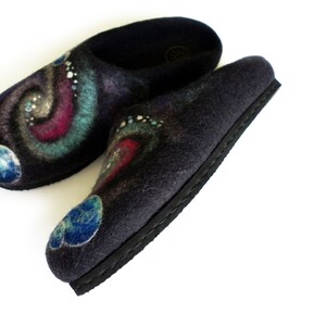 May include: A pair of black felt slippers with a galaxy design. The slippers have a blue, green, and pink swirl pattern with white dots and blue planets.