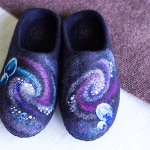 May include: A pair of dark blue wool slippers with a galaxy design. The slippers have a swirling pattern of purple, blue, and white, with small white dots representing stars.