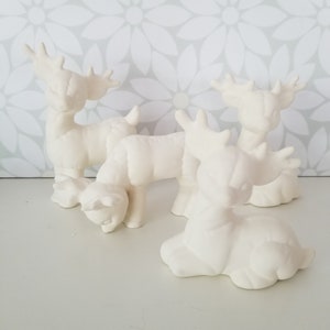 Könnte beinhalten: Drei weiße Keramik-Rentierfiguren. Die Rentiere sind in verschiedenen Posen, einschließlich Stehen und Liegen. Die Figuren sind unbemalt und bereit zum Dekorieren.