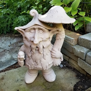 May include: A white ceramic garden gnome statue holding a mushroom and a small white object in its hand. The gnome has a long white beard and is wearing a hat.