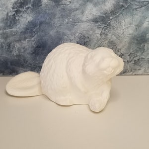 May include: White ceramic beaver figurine with a detailed textured surface. The beaver is sitting on its haunches with its tail behind it.