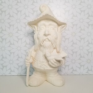 May include: White ceramic gnome figurine with a pointed hat, a long beard, and a bird in its hand. The gnome is holding a staff in its other hand.