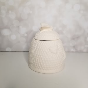 May include: White ceramic honey pot with a beehive design and a butterfly lid. The pot is textured to look like a honeycomb.