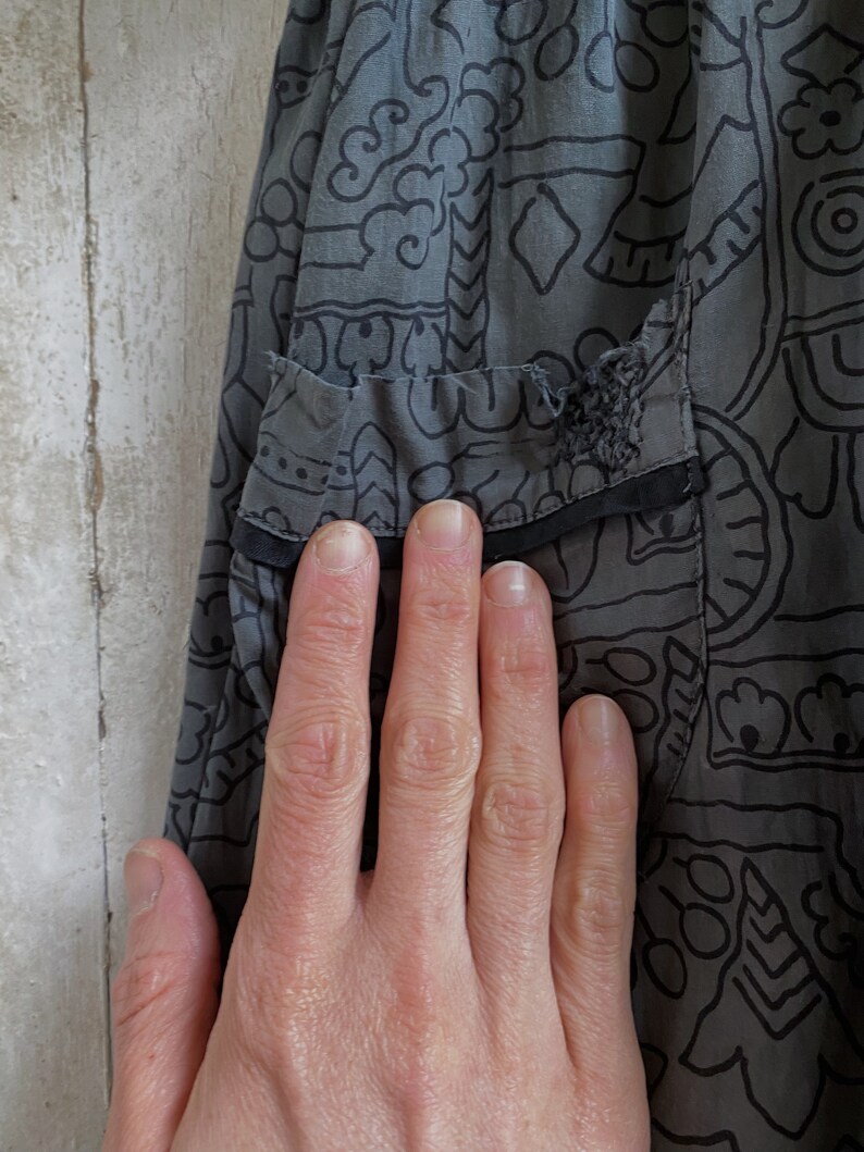 May include: Gray skirt with a black and white geometric pattern. The skirt has a small tear in the fabric.
