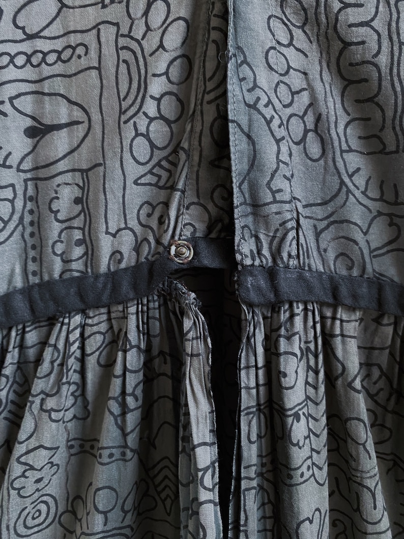 May include: A gray cotton dress with a black waistband and a black and white geometric print. The dress has a tie at the back.