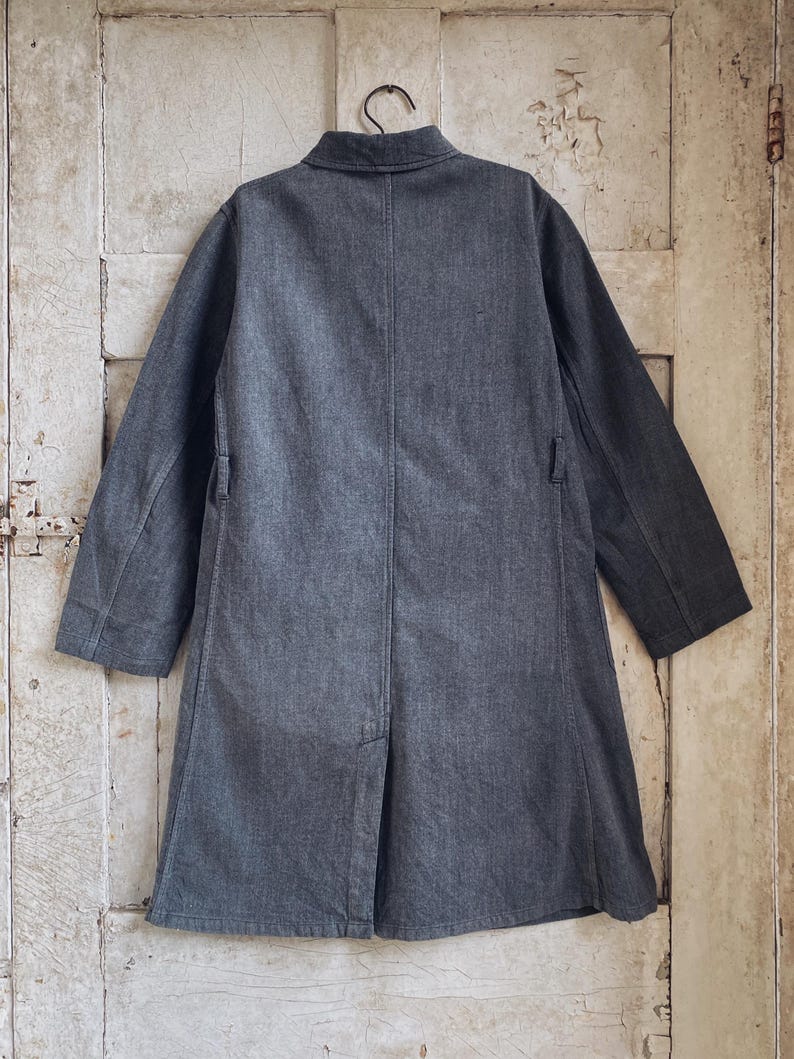 May include: A dark gray long-sleeved jacket with a collar and a single button closure. The jacket has a straight fit and a slightly longer length.